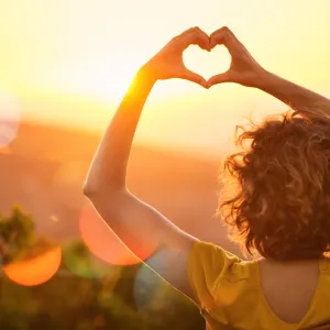 Woman making heart in sunrise